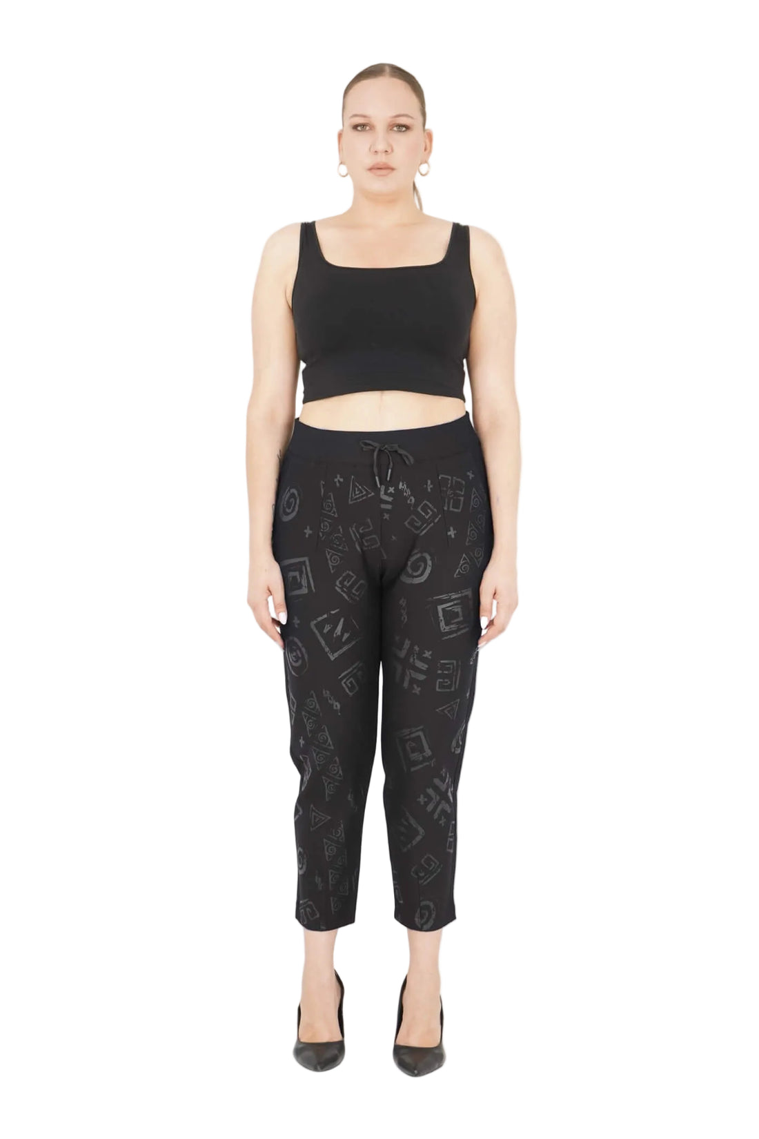 Woman wearing a black tank top and patterned black pants on a white background with 